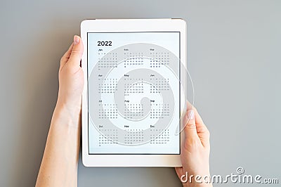 Tablet computer with an open app of calendar for 2022 year in a womans hands on a gray background. concept business or to do list Stock Photo