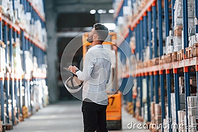 With tablet in hands. Storage worker is in the warehouse with bunch of products Stock Photo