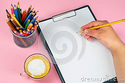 Tablet with white Leaf, next to which is a green plant, a glass with pencils. Hand holds a pen and writes a cup of coffee on the Stock Photo