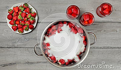 Tabletop photo - large steel pot of strawberries covered with crystal sugar, plate and glass bottles with more fruits around on Stock Photo