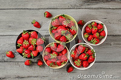 Tabletop view - five small bowls with strawberries, some of them spilled on gray wood desk Stock Photo