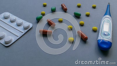 Tablets, caplets and thermometer on light gray background, yellow, green and orange pills on top right corner of the Stock Photo