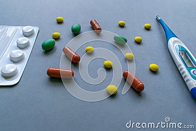 Tablets, caplets and thermometer on light gray background, yellow, green and orange pills on top right corner of the Stock Photo