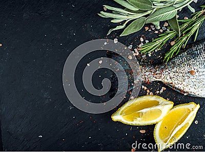 Tail of fresh raw Dorado or sea bream fish on black slate stone board with spices, herbs, lemon and salt Stock Photo