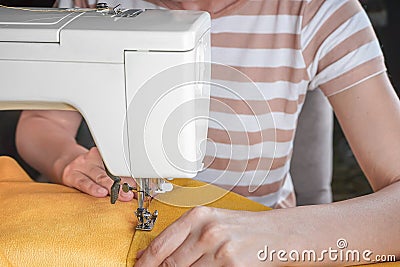 Tailor hands stitching yellow fabric on modern sewing machine at workplace in atelier Stock Photo