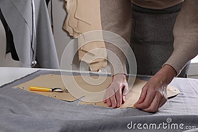 Tailor pinning sewing pattern to fabric at table in atelier, closeup Stock Photo