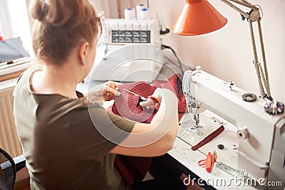 Tailor woman sitting on workplace in atelier and using scissors for cutting off cloth piece in sewing process. Back view Stock Photo