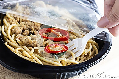 Take-away food ready meal: Woman hands holding fork and open cling wrap with take out food in plastic boxes on wood background. C Stock Photo