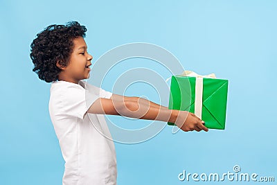Take this present! Side view of cheerful generous good-natured little boy with curls offering gift box Stock Photo