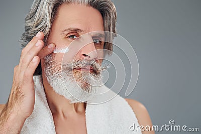 Taking care of face and skin clearness. Stylish modern senior man with gray hair and beard is indoors Stock Photo