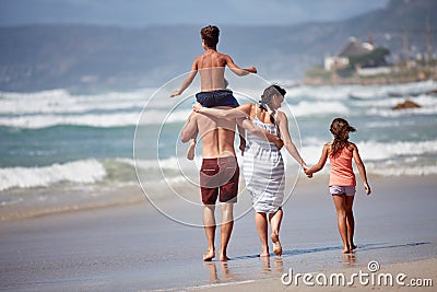 Taking a family beach stroll. Rearview shot of a family walking along the beach. Stock Photo