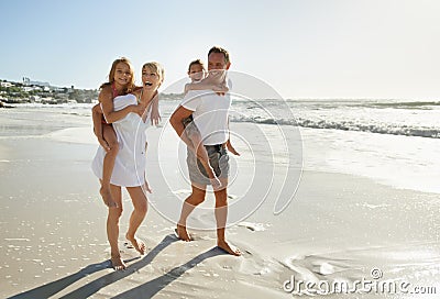 Taking a family beach stroll. Smiling parents carrying their son and daughter down the beach. Stock Photo