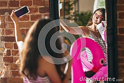 Happy young girl trying on new outfits, preparing for summer vacation standing in front of mirror at home, indoors Stock Photo