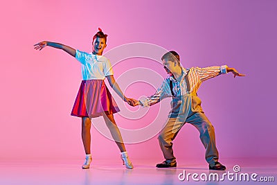 Talented, artisitc children, boy and girl in retro clothes dancing lindy hop against pink studio background in neon Stock Photo