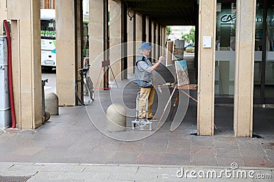 Retired male artist, senior man painter draws on canvas, standing in Freedom central square, piazza della liberta. Udine Editorial Stock Photo