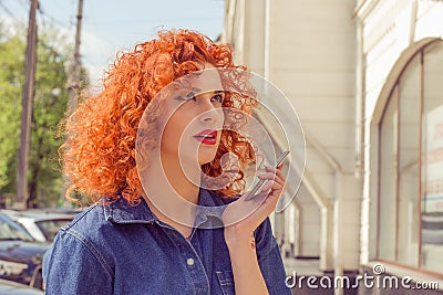 Talk to my hand. Annoyed woman with red curly hair holding mobile phone in hand ignoring conversation looking up frustrated Stock Photo