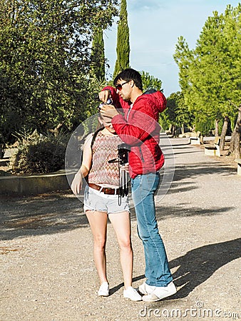 A tall dark-haired man takes off sunglasses entangled in blonde hair of a young woman with a camera Stock Photo
