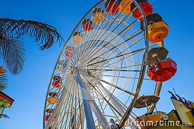 A tall metal Ferris wheel with colorful cars around the wheel on with blue sky the Santa Monica Pier Editorial Stock Photo