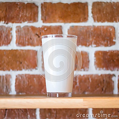 Tall mug on vintage brick wall background. Wooden display shelf for showing transparent drink cup in grunge concept. Brickwork Stock Photo