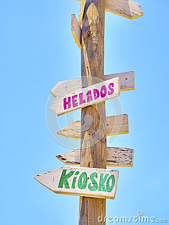 Tall post with colored wooden signboards pointing to various destinations and a beach services in Spanish Stock Photo