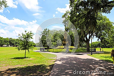 A tall tower shaped monument in the park surrounded by lush green grass and weeping willow trees with blue sky and clouds Editorial Stock Photo