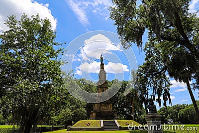 A tall tower shaped monument in the park surrounded by lush green grass and weeping willow trees with blue sky and clouds Editorial Stock Photo