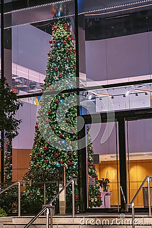 Tall and well decorated fir tree for Christmas or New Year celebrations in a hall of a huge office building. Rich company with Stock Photo