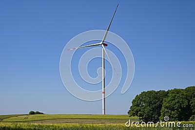 Tall wind turbine with a slender tower and three rotor blades standing on a field in a rural landscape against the blue sky, Stock Photo