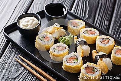 Tamagoyaki set sushi roll with rice, omelette, cheese, salmon and avocado served with sauces, wasabi and ginger on a plate. Stock Photo
