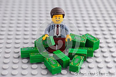 Lego businessman minifigure standing in a pile of cash Editorial Stock Photo