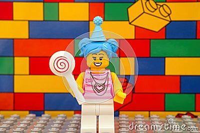 A Lego blue hair girl minifigure with a lollipop against colour brick wall background Editorial Stock Photo