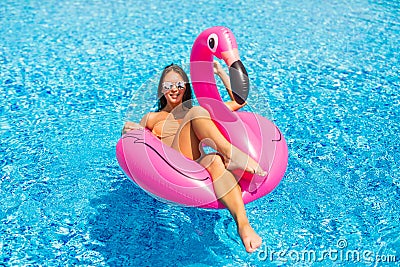 Tan girl sits on inflatable mattress flamingos and relax in the pool. Pool party Stock Photo