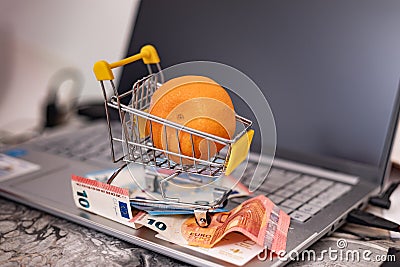 Tangerine in a basket and banknotes on a laptop keyboard Stock Photo