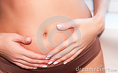 A tanned girl holds her hands to her stomach. IVF concept, pregnancy, digestion, health of the female reproductive system. Stock Photo