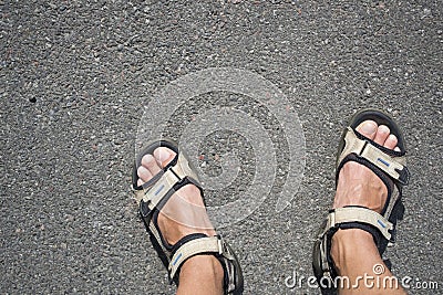Tanned male legs in hiking sandals on the asphalt on a sunny day. Stock Photo