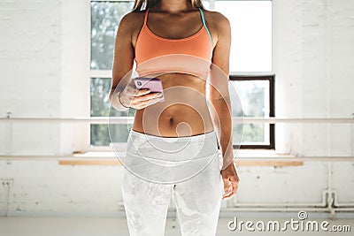 Tanned sporty woman wearing sportwear in white sunny gym hold smartphone in hand and counts calories in fitness application fater Stock Photo