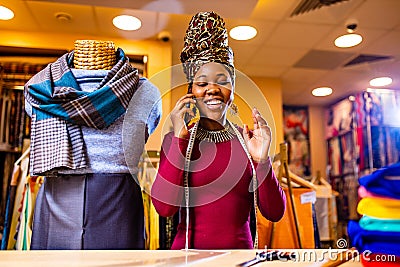 tanzanian woman with snake print turban over hear working in fabrics shop calling to client by smartphone Stock Photo