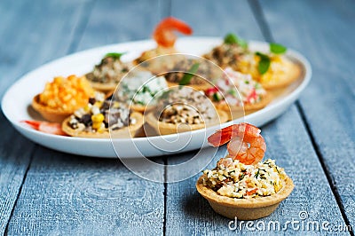 Tartlets with salads and shrimps on a white plate on wooden table Stock Photo