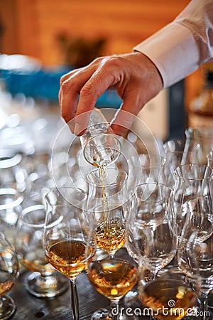 Tasting cognac or brandy. Glasses with brandy or cognac stand in a row. The waiter pours cognac into glasses, close-up. Stock Photo