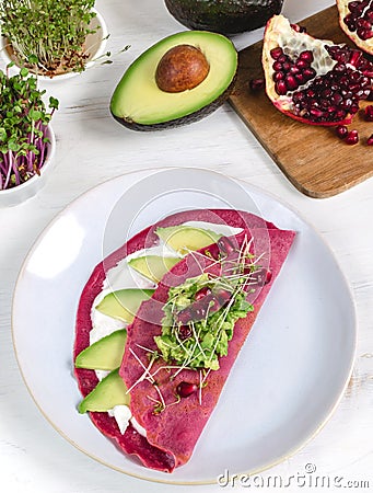 Tasty appetizing beetroot pancakes served on plate with avocado, sprouts and pink radish, white wooden table Stock Photo