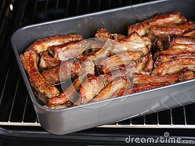 Tasty baked pork ribs in a black baking tray in an oven Stock Photo