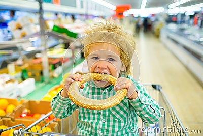 Tasty bun. Boy bites bagel with sesame in the supermarket. Bakery products. Shopping Shopping for food. Child food Stock Photo