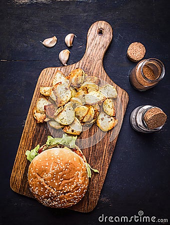 Tasty burger on cutting board with potato wedges with salt and pepper and garlic wooden rustic background top view close up Stock Photo