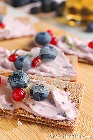 Tasty cracker sandwiches with cream cheese, blueberries, red currants and honey on wooden board, closeup Stock Photo