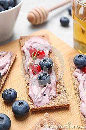 Tasty cracker sandwiches with cream cheese, blueberries, red currants, thyme and honey on wooden board, closeup Stock Photo