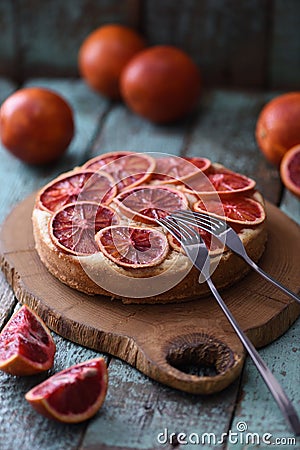 Tasty domestic dessert. Blood orange cake with raw oranges on oak cutting board over shabby rustic blue table Stock Photo