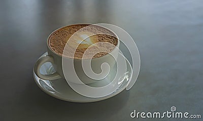 Tasty drinking, a cup of capuccino coffee decorated with heart pattern on brown milk froth in white ceramic cup on gray table Stock Photo