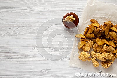 Tasty fastfood: fried potato wedges, chicken bites, bbq sauce on a white wooden surface, top view. Flat lay, overhead, from above Stock Photo