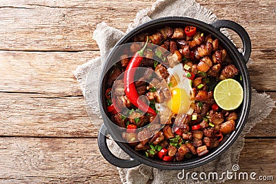Tasty filipino sisig food served with egg, lime and chili pepper close-up in a pan. Horizontal top view Stock Photo