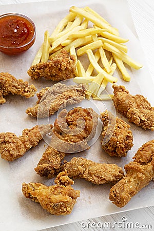 Tasty fried chicken drumsticks, spicy wings, French fries and chicken fingers with sour-sweet sauce on baking sheet over white woo Stock Photo